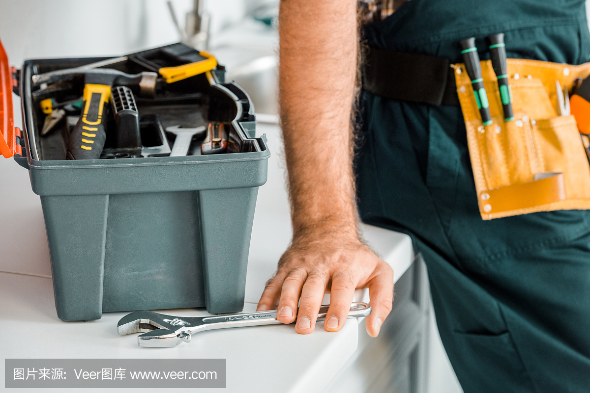 裁剪圖像水管工靠在廚房柜臺和觸摸可調節扳手在廚房
