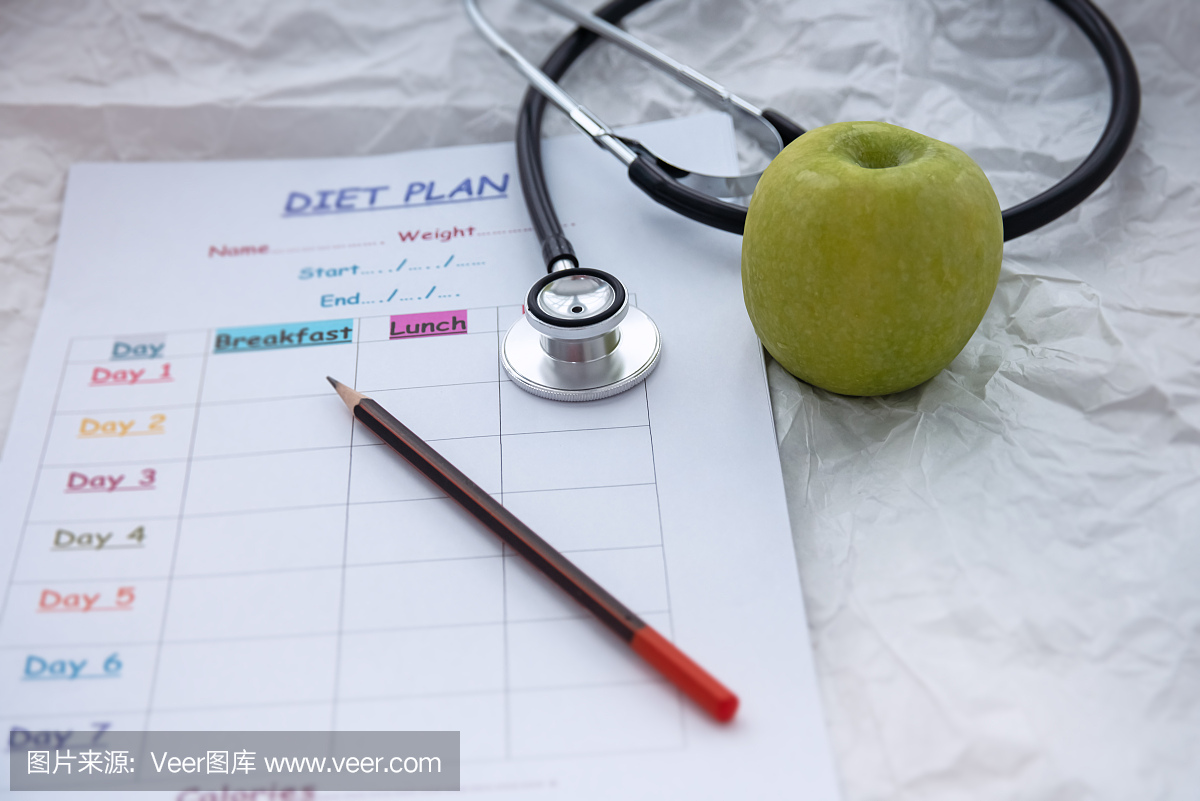 聽診器和青蘋果旁邊放著模糊的飲食時間表計劃,背景上,燈光周圍模糊,保健理念